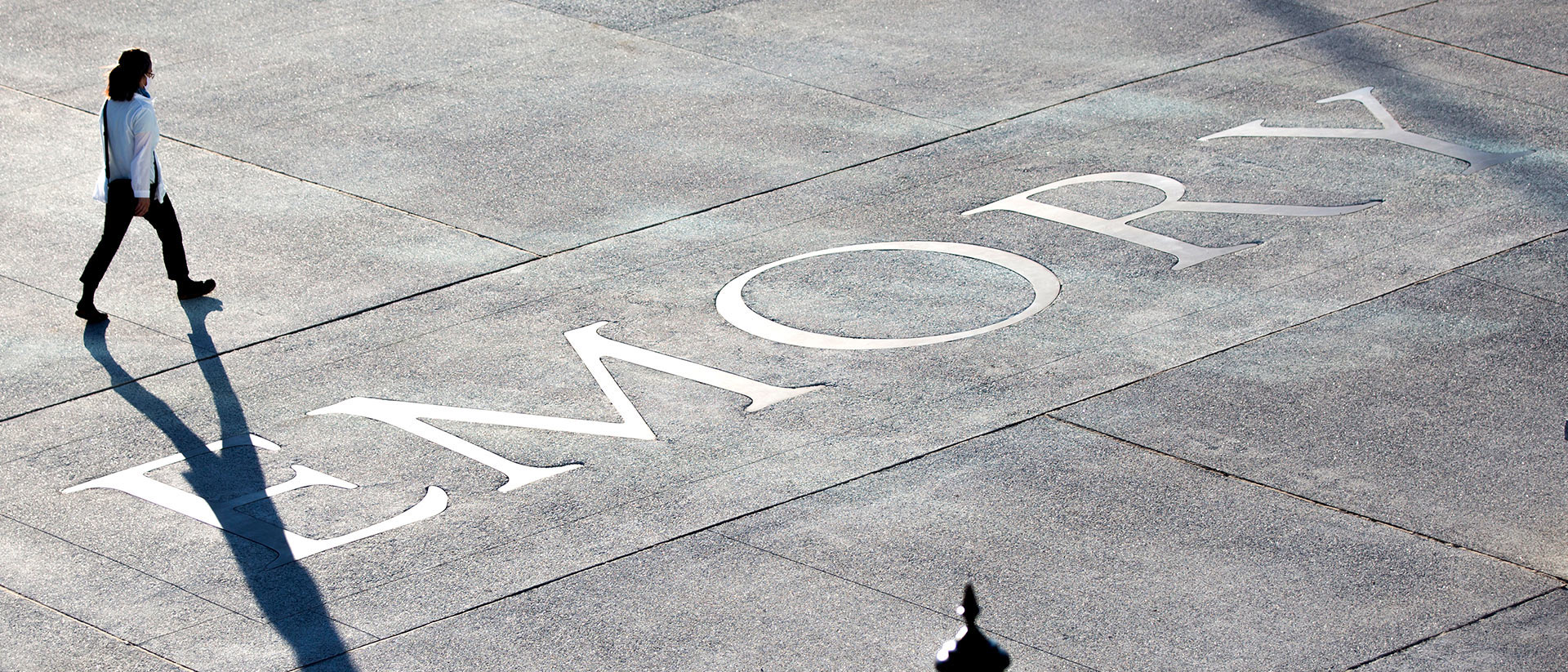 A person walking on a sidewalk inset with the Emory logo