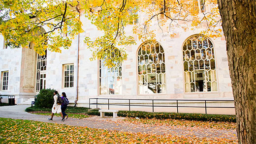 An autumn scene with two students walking in front of Emory's Convocation Hall with yellow fall leaves around them