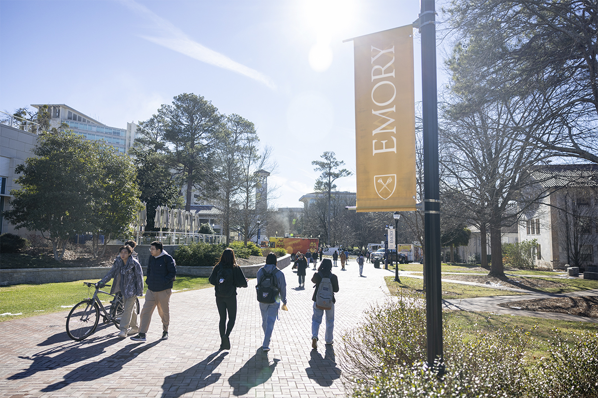 an image of students walking on a college campus with a lightpole banner that reads Emory