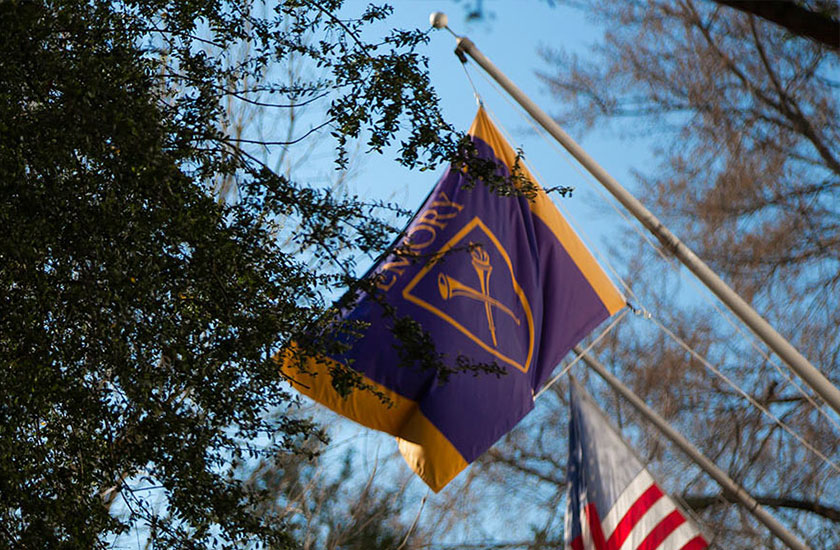 Emory flag with blue sky and trees behind it and part of the US flag