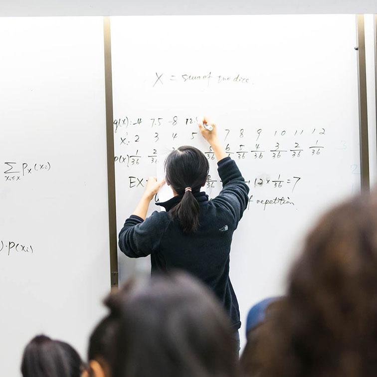 Emory professor writing on a whiteboard before a classroom of students