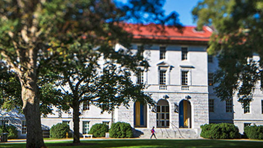 campus building on quad with red roof and green grass and person walking by